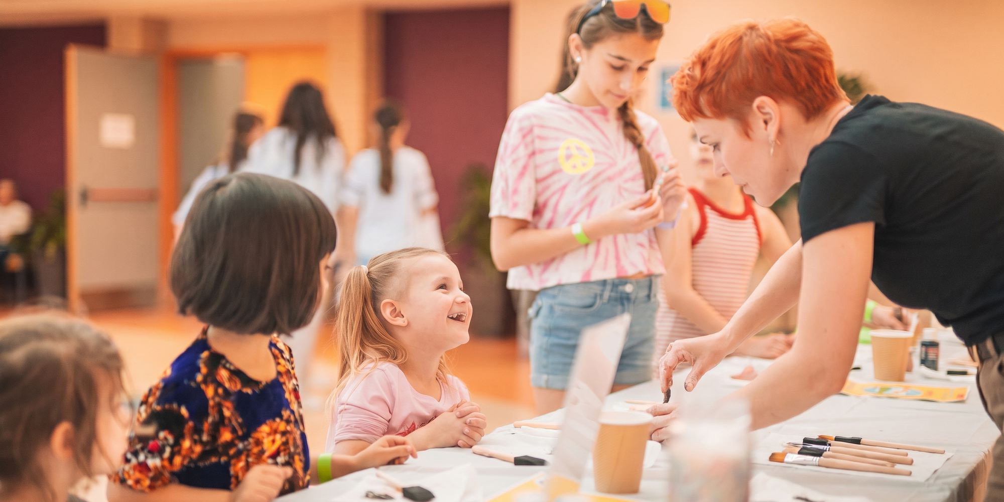 A teacher leaning in to help two young children at a craft table.