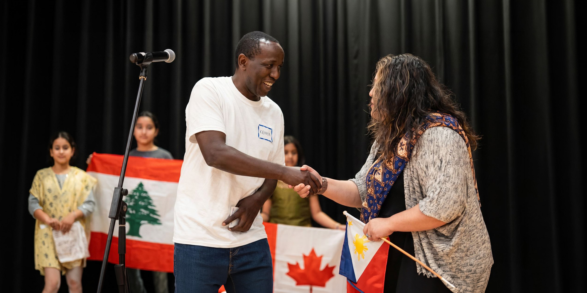 Two people shaking hands at a microphone in front of national flags.